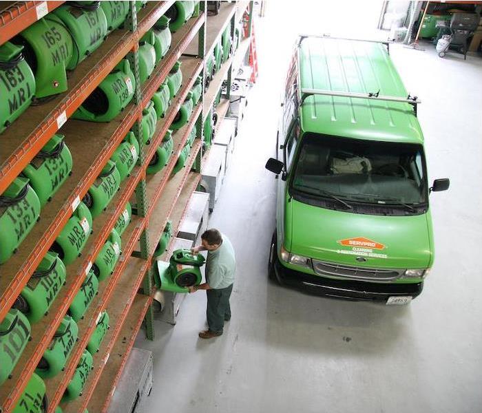 A green SERVPRO van parked in a warehouse full of equipment.